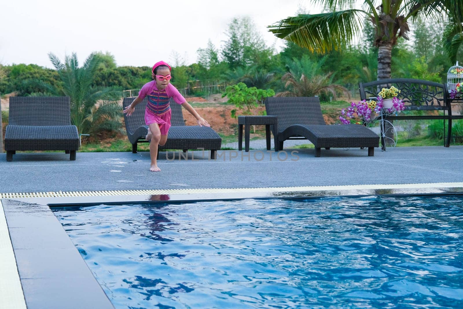 Cute girl with goggles jumping into the pool. Little girl swimming and playing in the water. summer vacation concept.