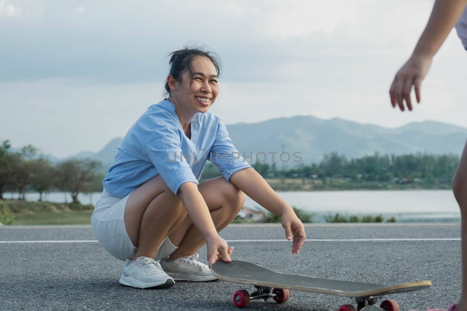 Mother teaching her daughter how to skateboard in the park. Child riding skate board. Healthy sports and outdoor activities for school children in the summer. by TEERASAK