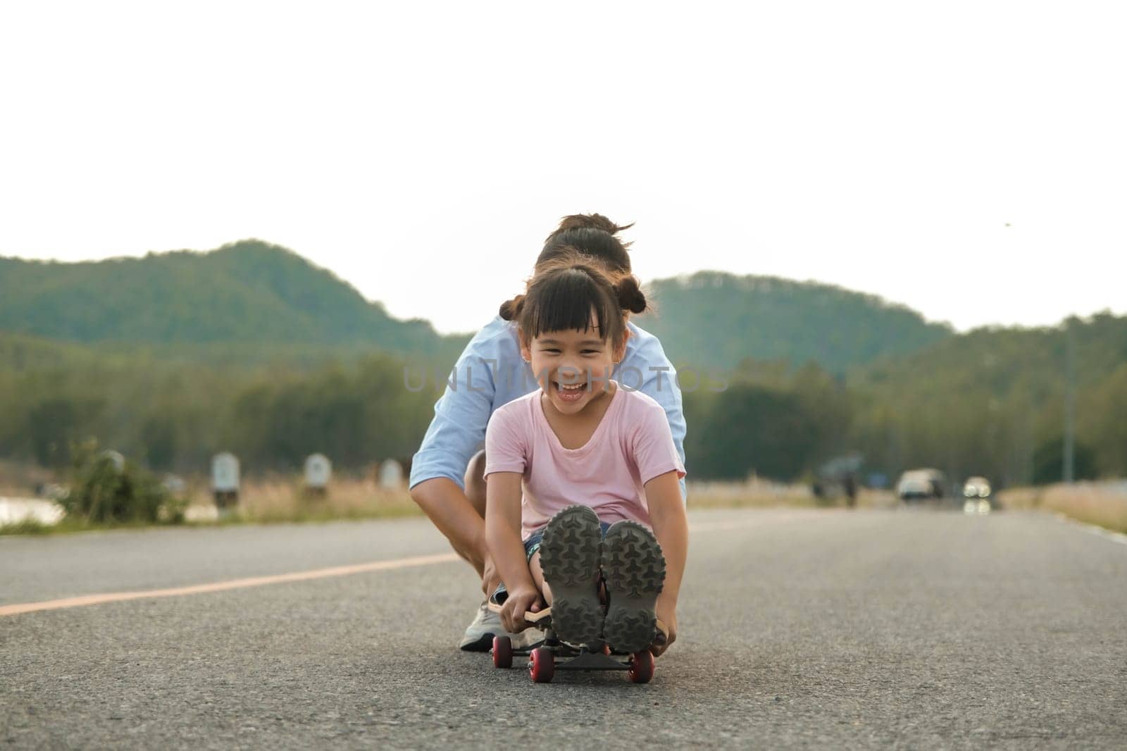 Mother teaching her daughter how to skateboard in the park. Child riding skate board. Healthy sports and outdoor activities for school children in the summer. by TEERASAK