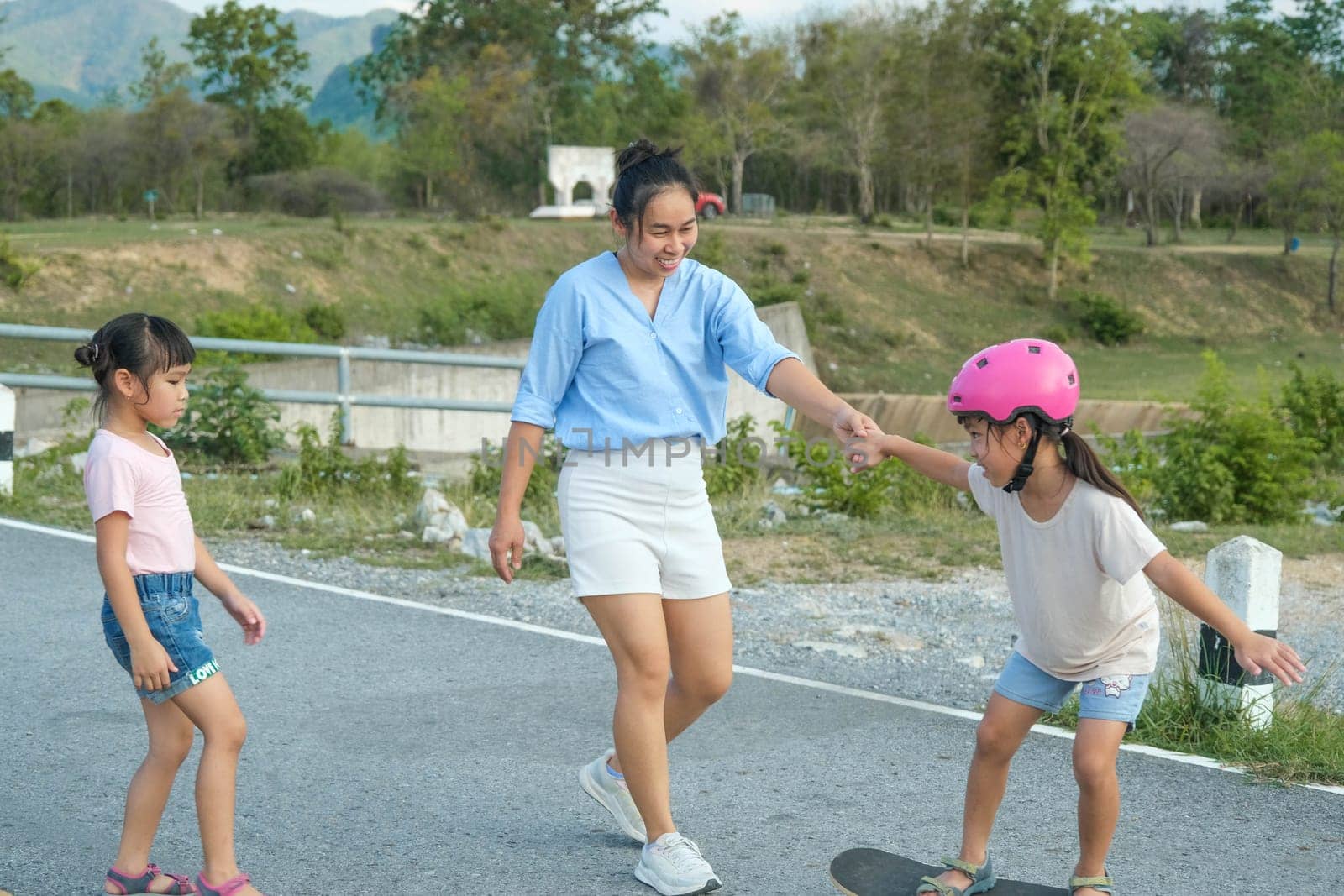 Mother teaching her daughter how to skateboard in the park. Child riding skate board. Healthy sports and outdoor activities for school children in the summer.