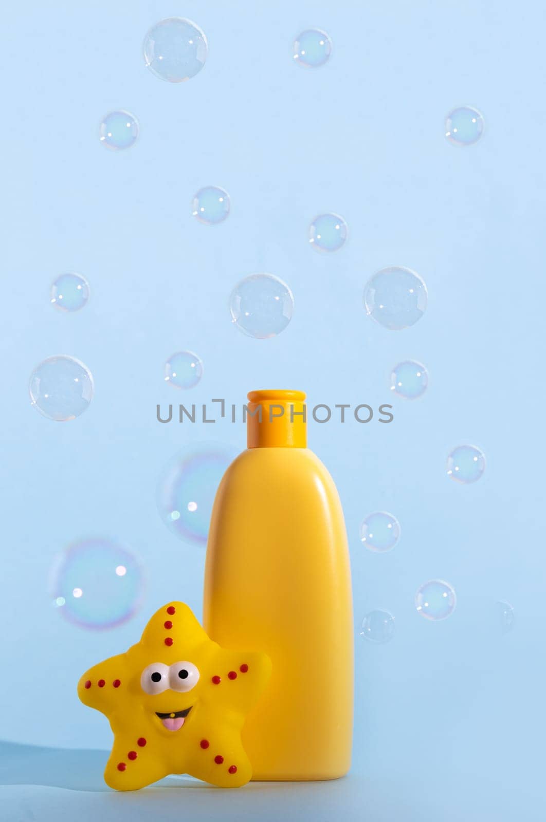 Empty bottle of baby washing gel, bath foam, liquid soap or shampoo with yellow star fish and flying soap bubbles. Children's hygiene. Template for design