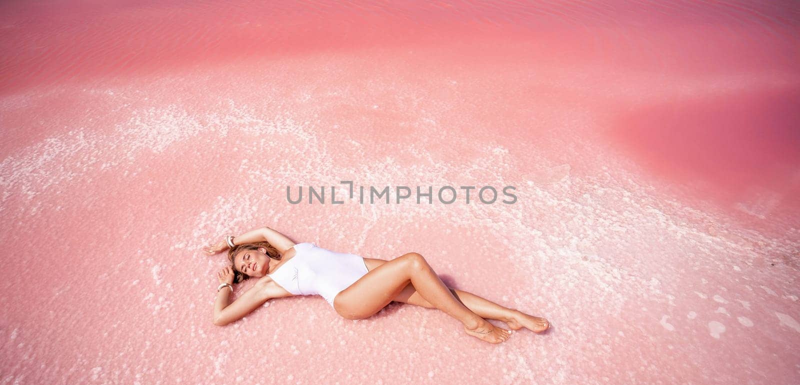 Woman in a pink salt lake. She lies in a white bathing suit. Wanderlust photo for memory by Matiunina