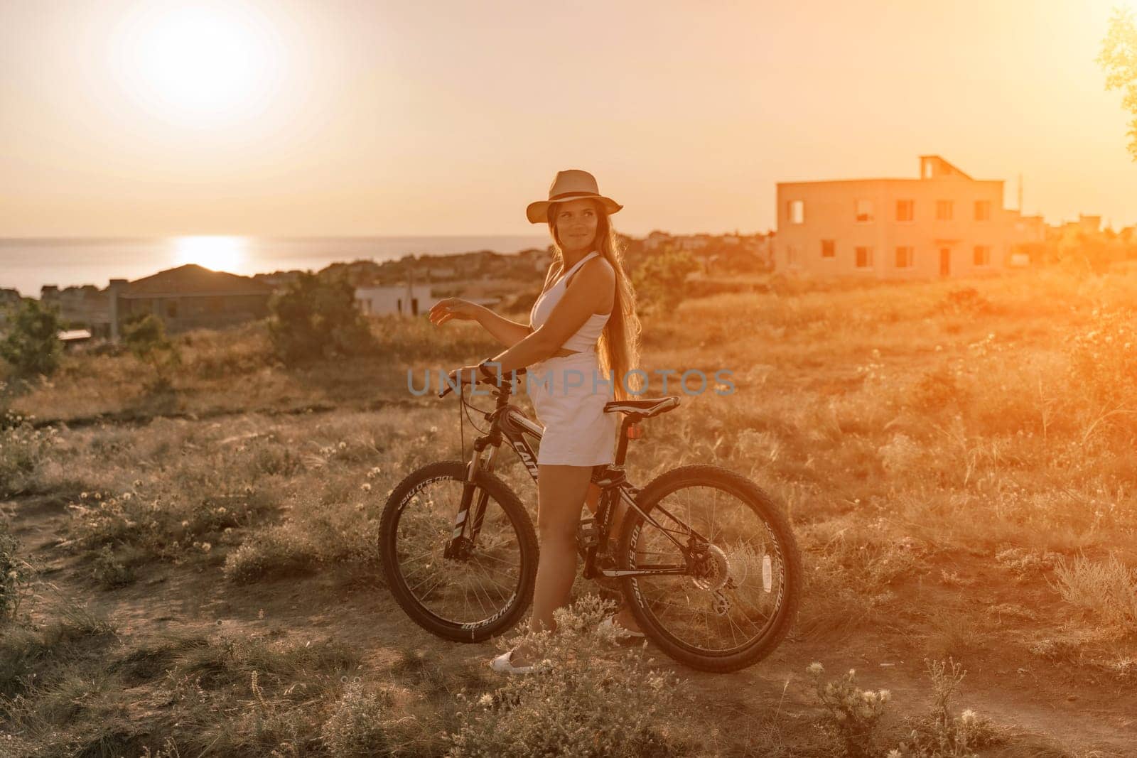 Woman travel bike. Happy woman cyclist sitting on her bike, enjoying the beautiful mountain and sea landscape, signifying the idea of an adventurous bike ride