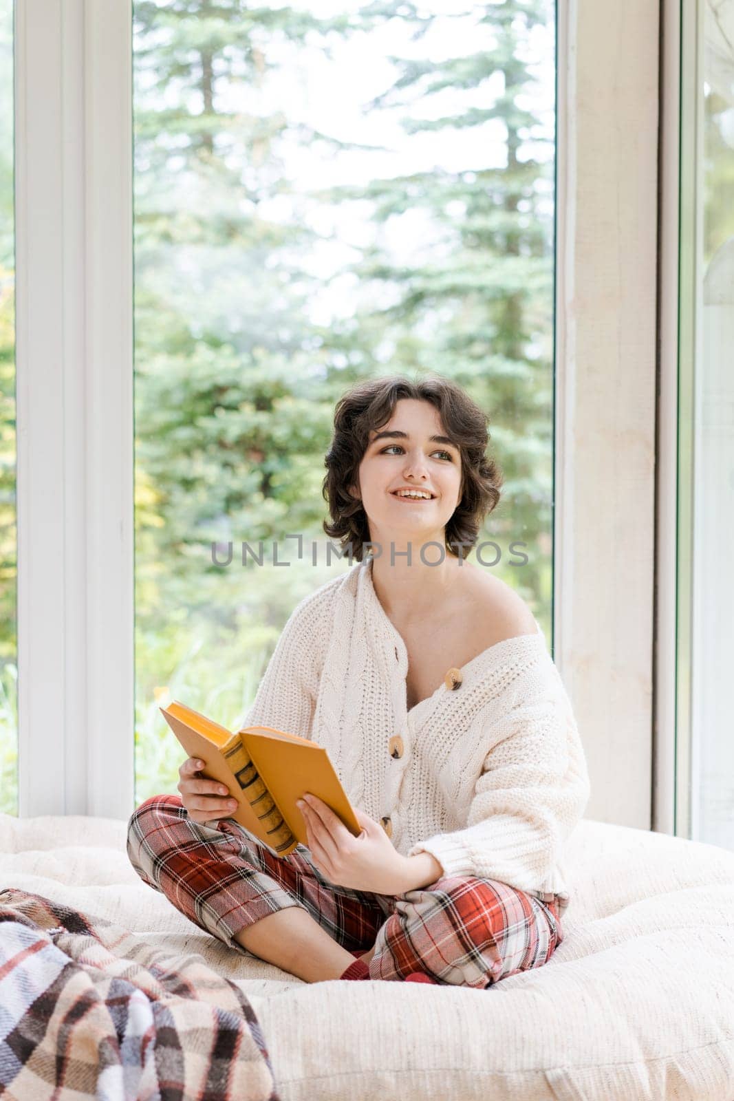 Brunette woman in warm sweater reading book sitting on room on the veranda by EkaterinaPereslavtseva