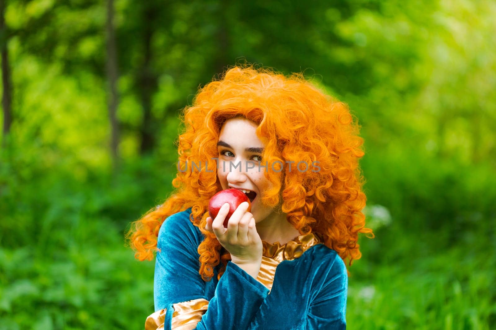 Curly red-haired girl fairy in nature with long curly hair in a blue dress eats by EkaterinaPereslavtseva