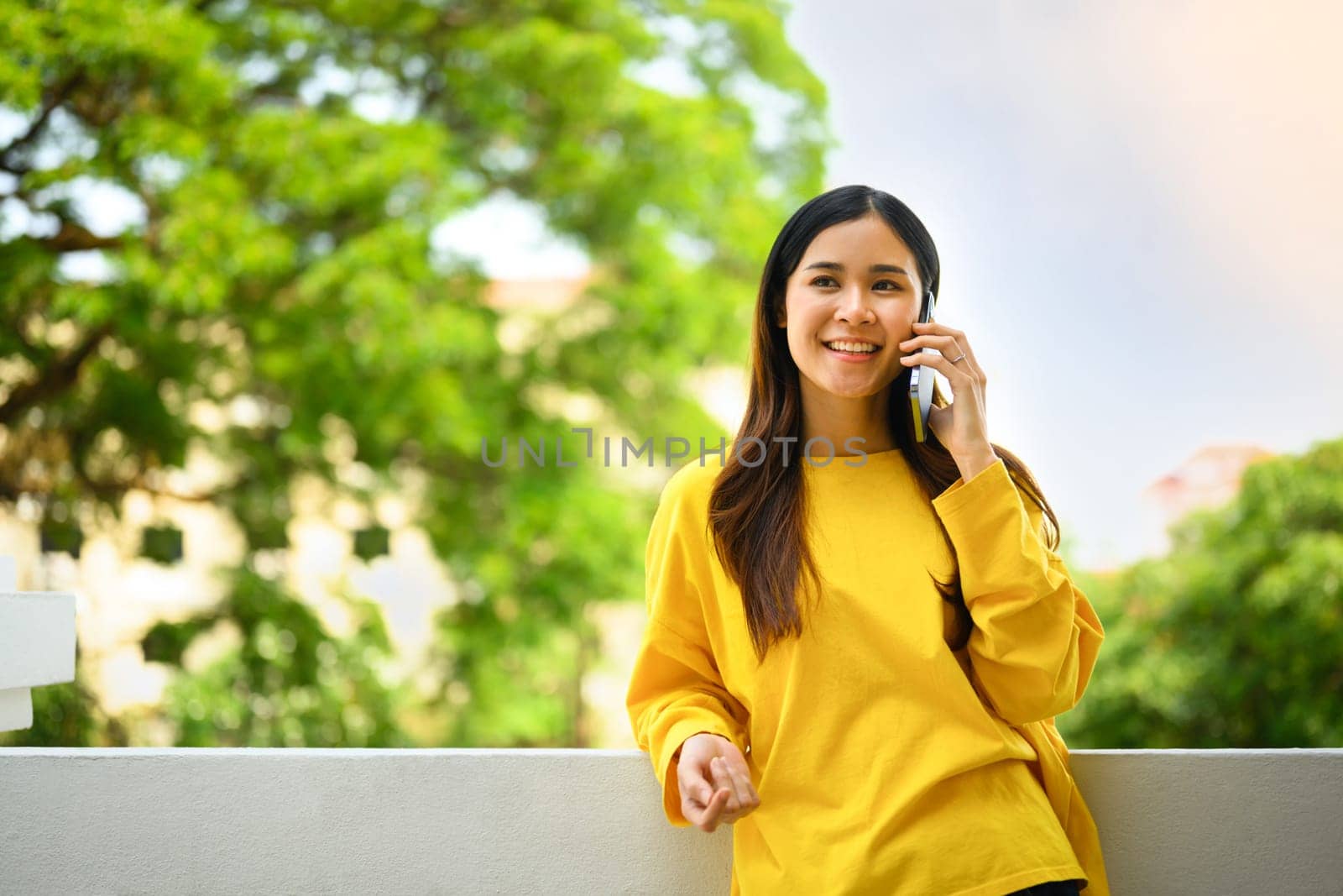 Attractive young woman talking to friends on mobile phone while standing on the balcony of office building.