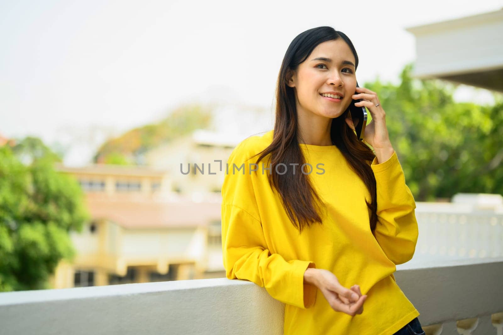 Pleasant young woman standing on the balcony of a modern office and talking on mobile phone.