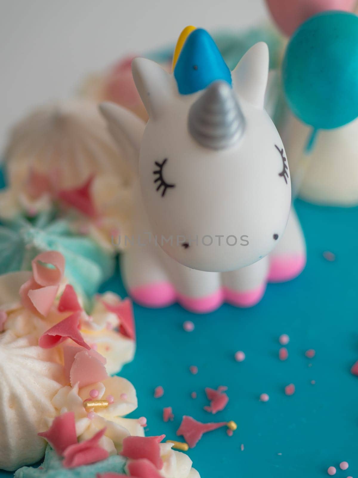 studio shot of chocolate frosted blue dripped icing white cup cake, unicorn , meringue and sprinkles on top