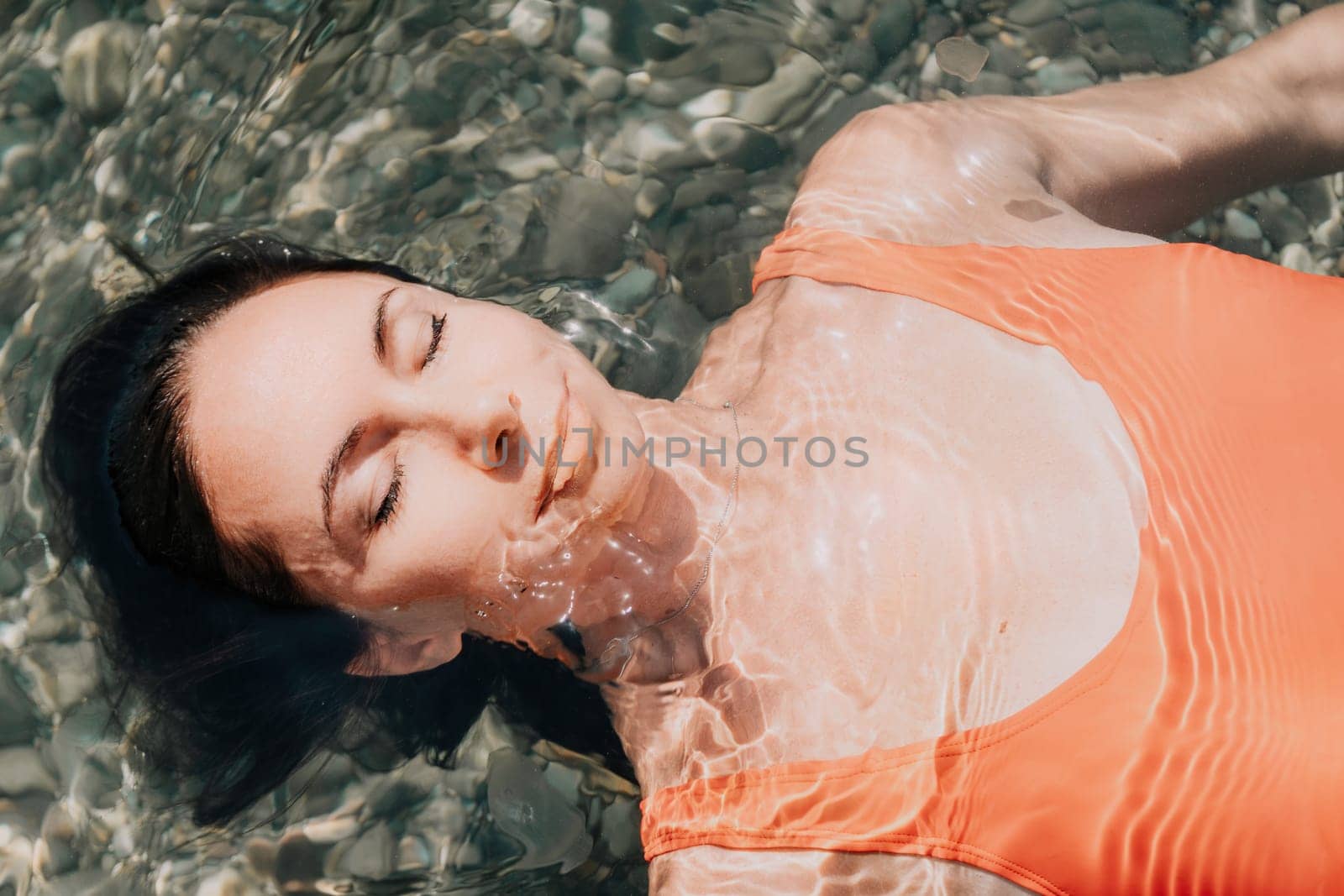 Woman travel portrait. Close-up portrait of a happy woman with long hair in a red bikini, floating in water and smiling at the camera. by panophotograph