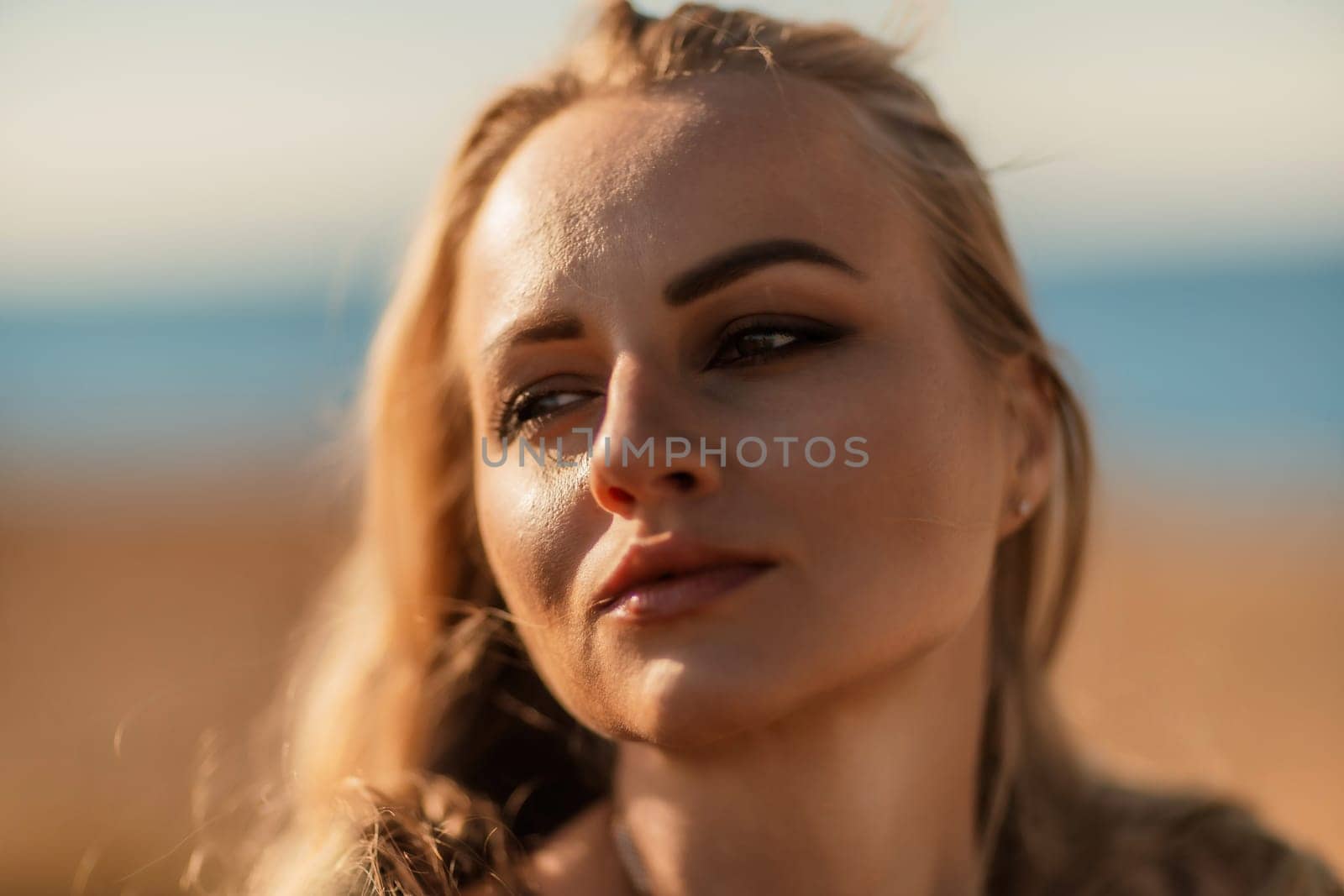 Portrait blonde sea cape. A calm young blonde in an unbuttoned khaki raincoat stands on the seashore, under the raincoat there is a black skirt and top.