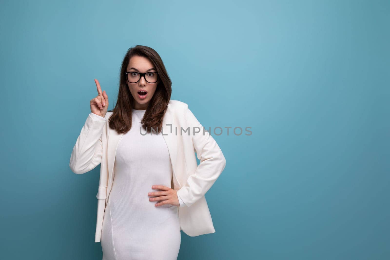 positive young business brunette woman in white office dress on blue studio background.