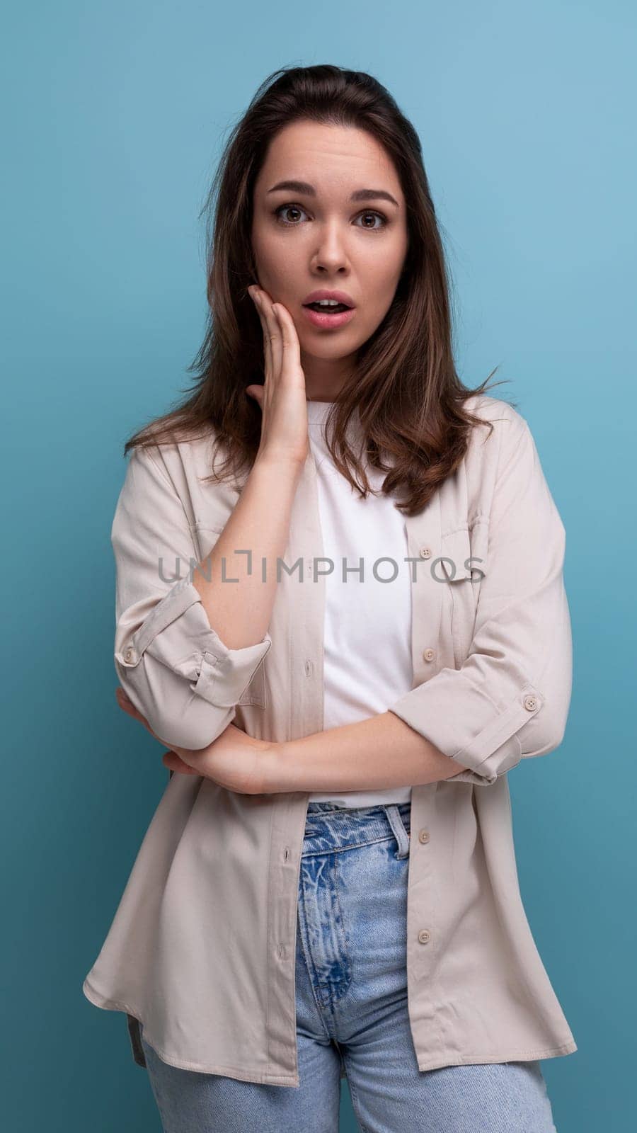 distressed brunette 30 year old female person dressed in shirt and jeans looking at camera on blue background.