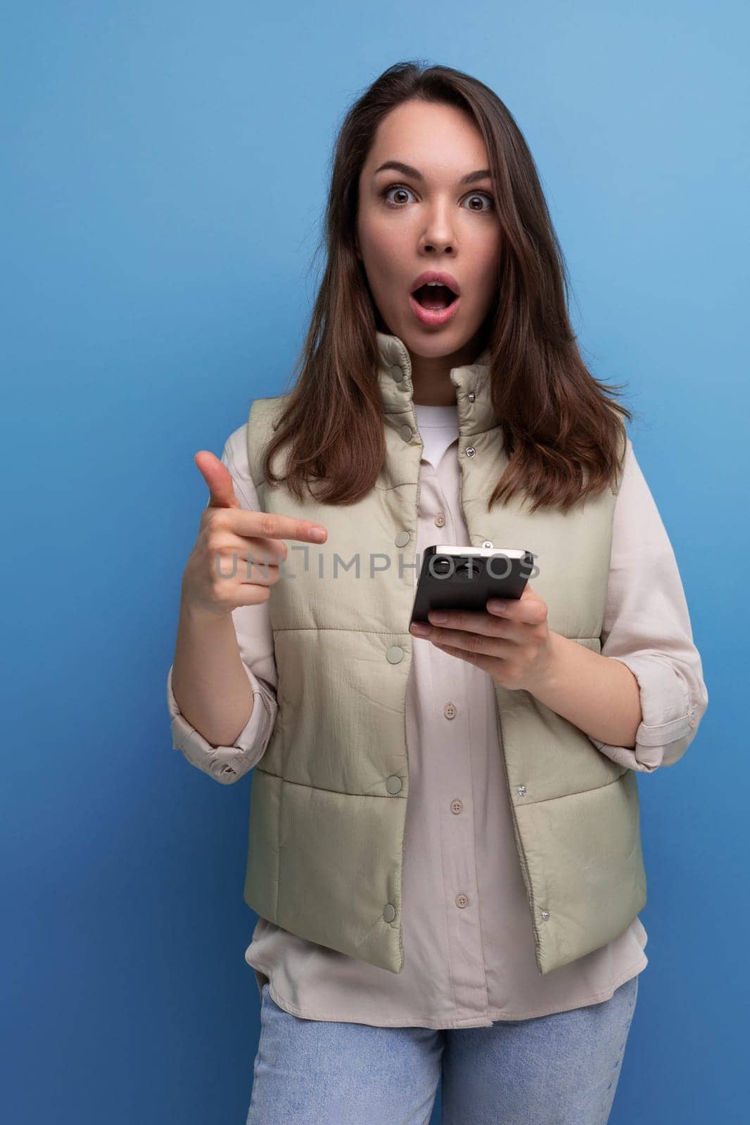 surprised brunette young woman with a mobile phone in her hands on a studio background.