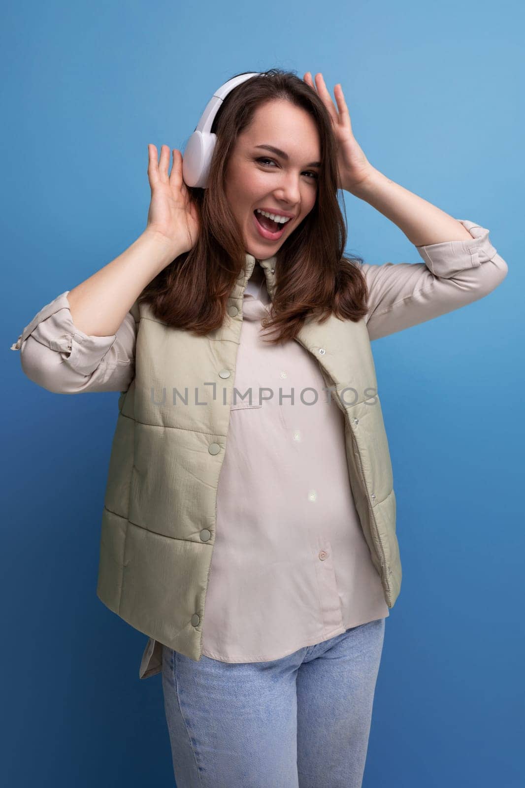 cheerful young lady brunette dances listening to music in headphones on a studio background.