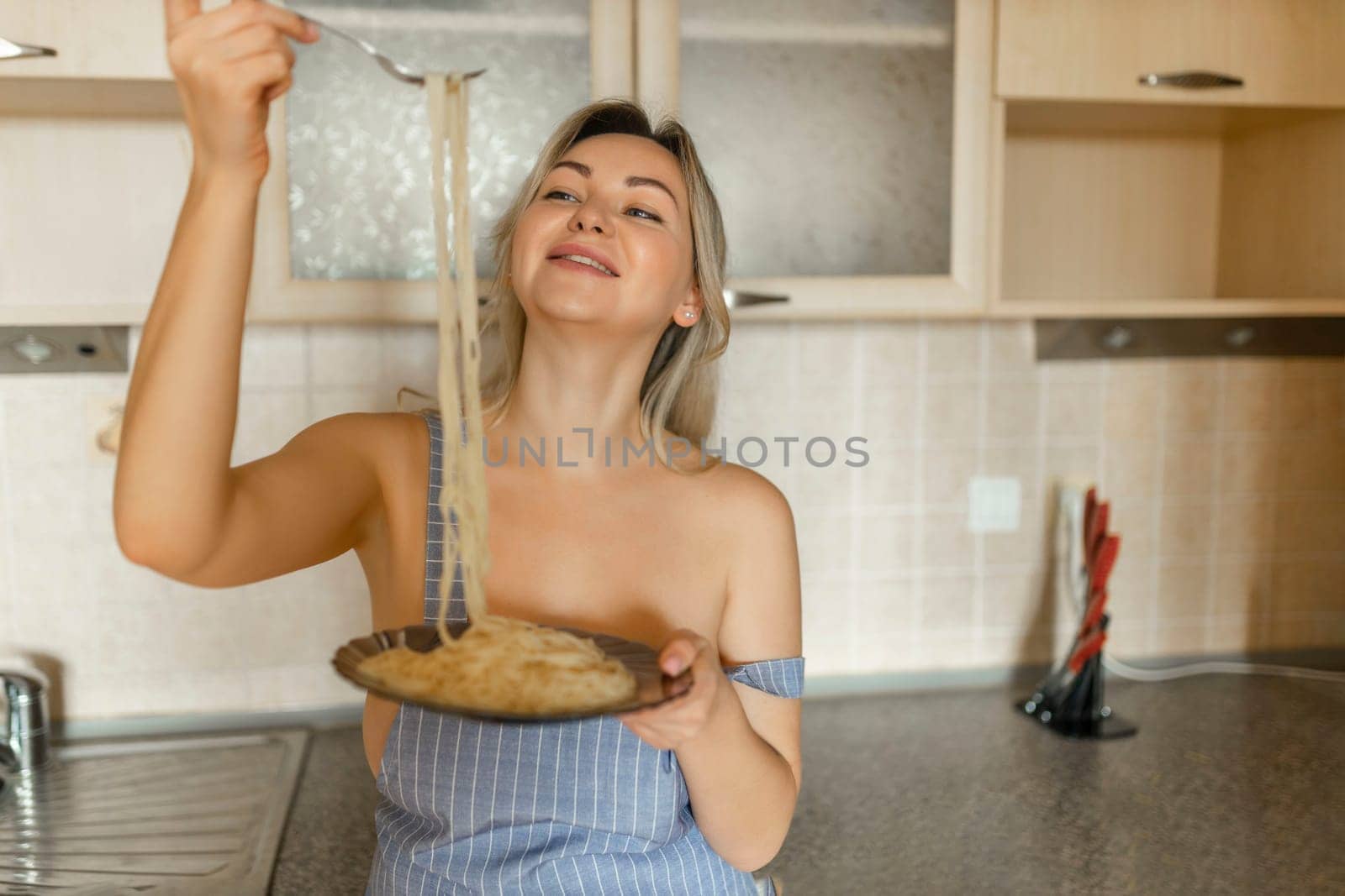 Sexy blonde housewife eating cooked pasta portrait close-up.