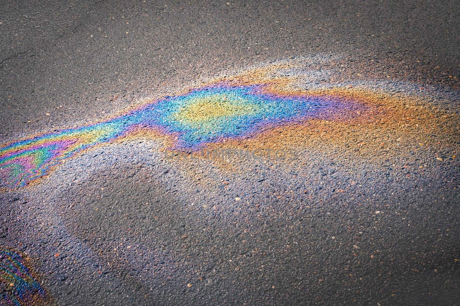 Oil stains on wet asphalt. Puddles are contaminated with multicolored streams of oil.