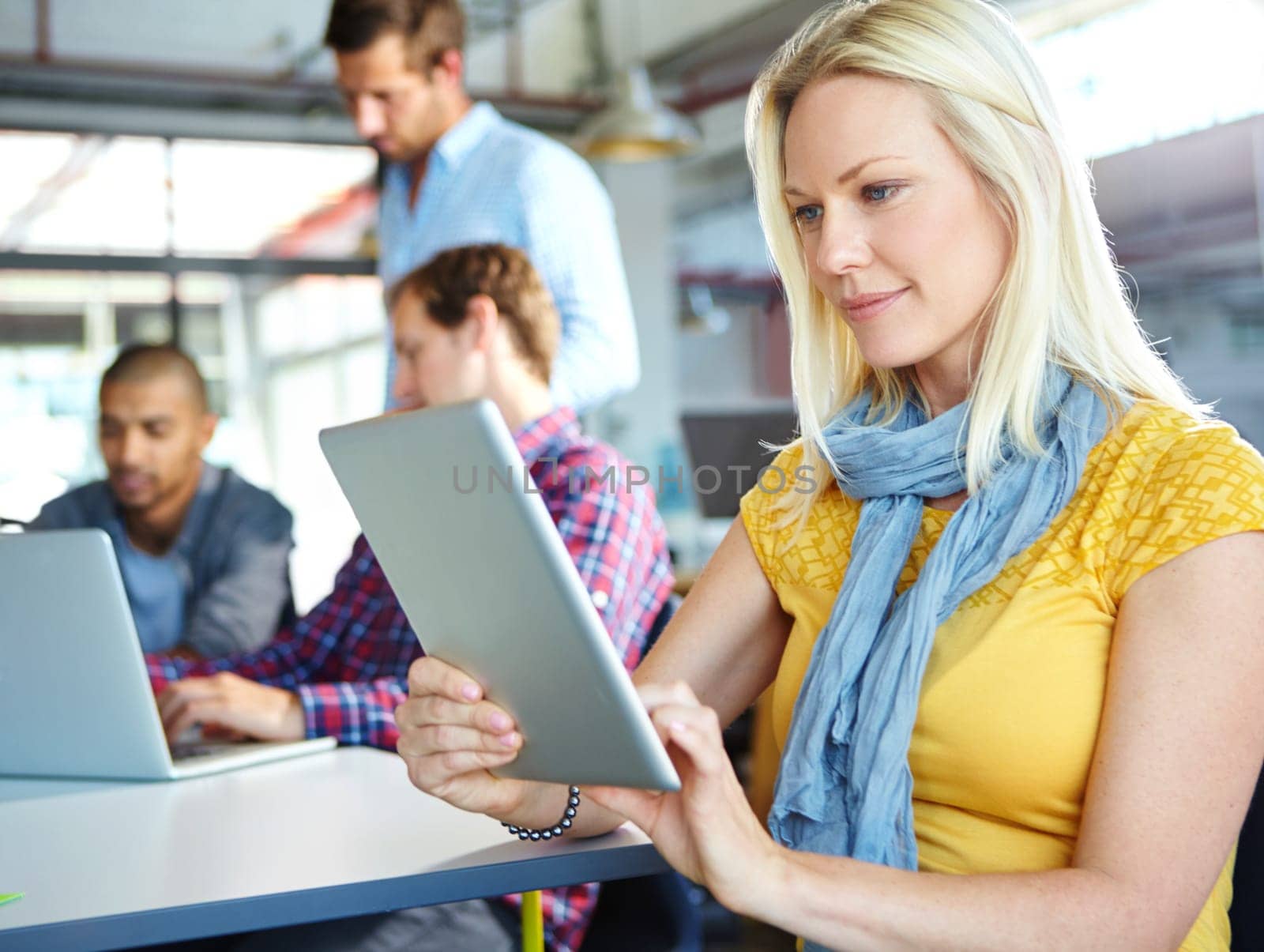 Going to her online resources. a young designer using a digital tablet with colleagues in the background