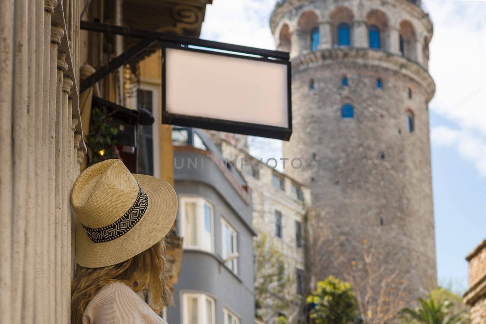 A girl in a hat looks at the Galata tower, and above it hangs a mockup with an empty space for the logo.