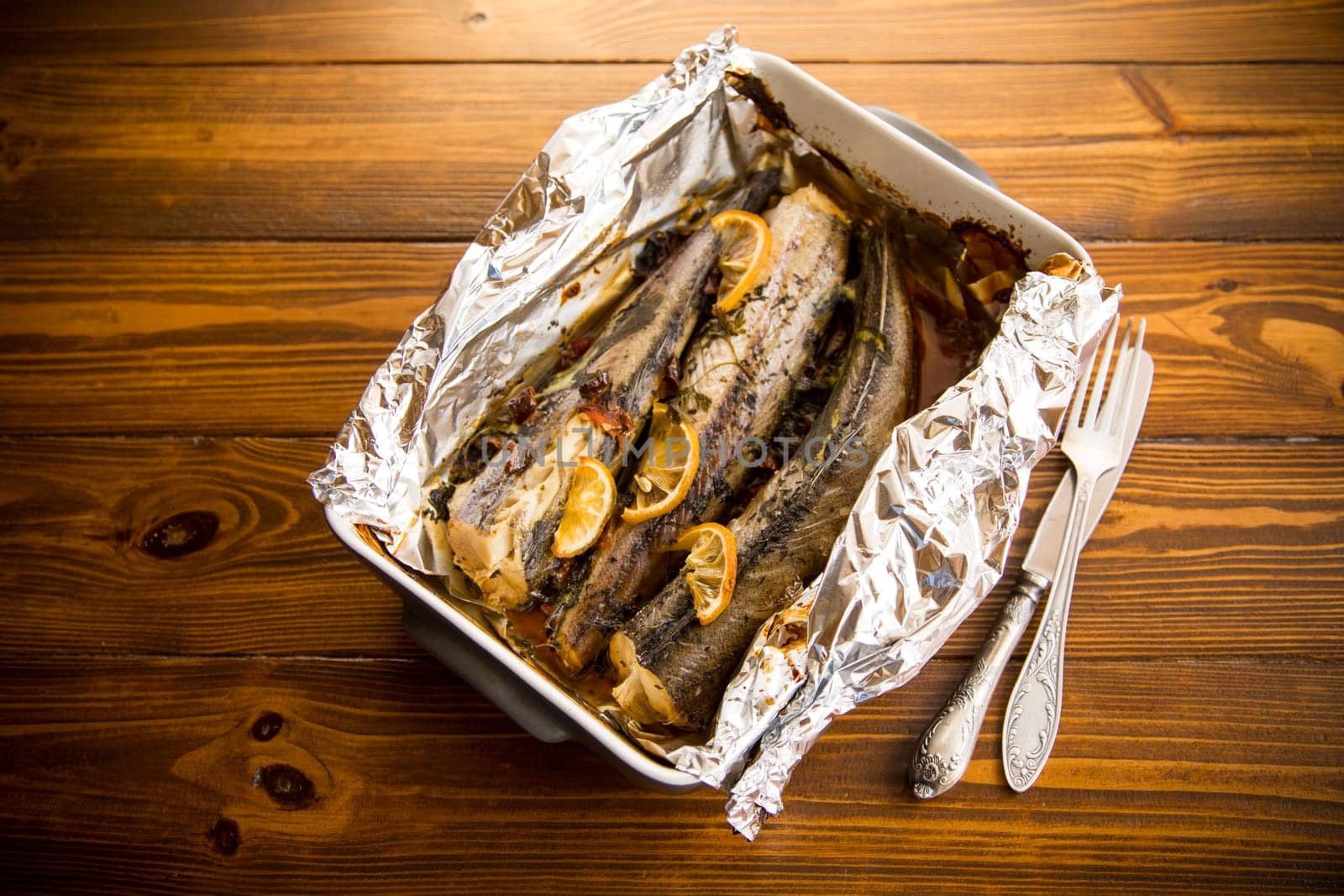 Baked fish with seasonings and spices in foil, in a ceramic form.