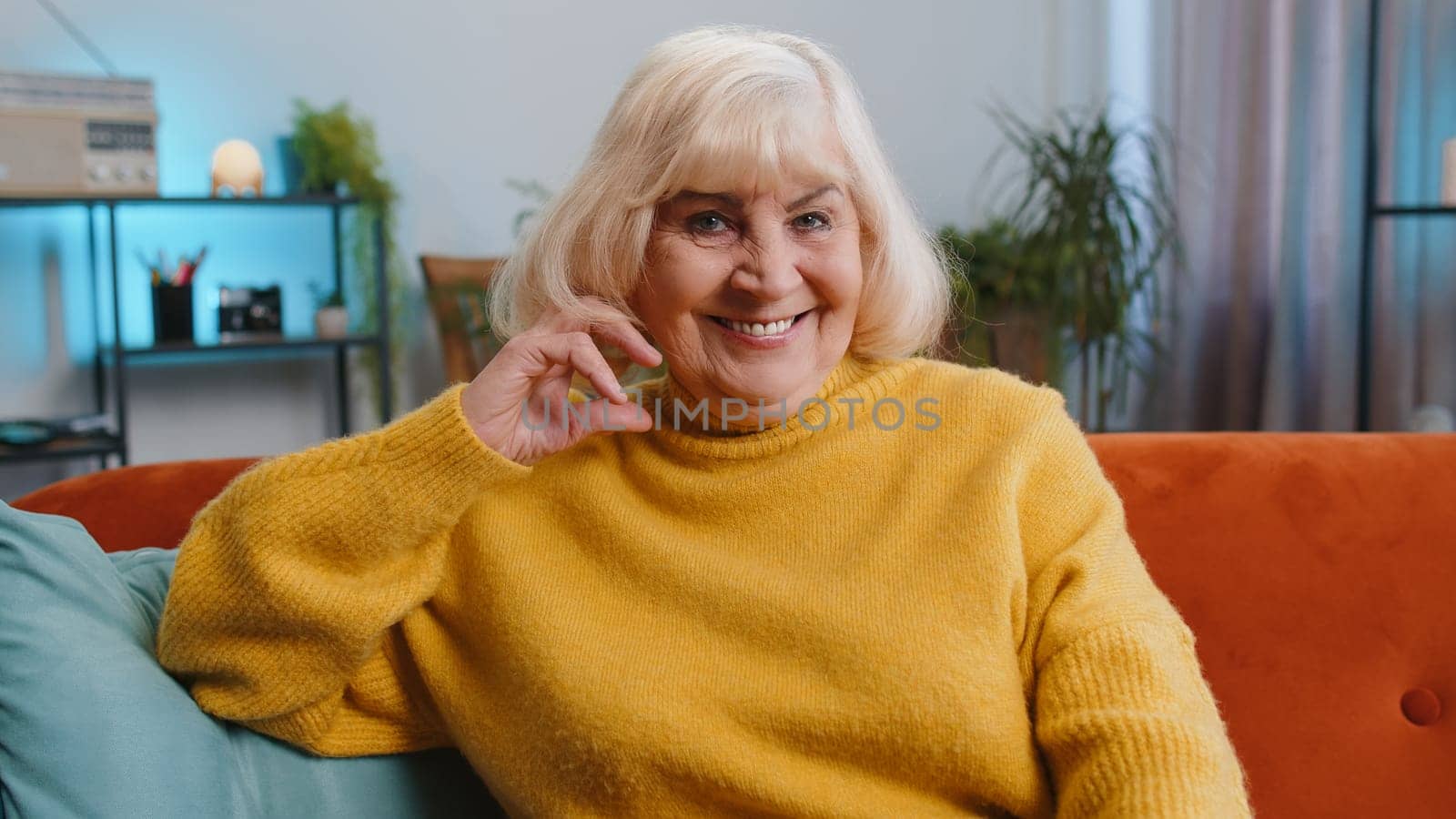 Happy calm senior woman at home couch smiling friendly, glad expression looking away dreaming resting, relaxation feel satisfied concept good news, celebrate win. Elderly grandmother in living room