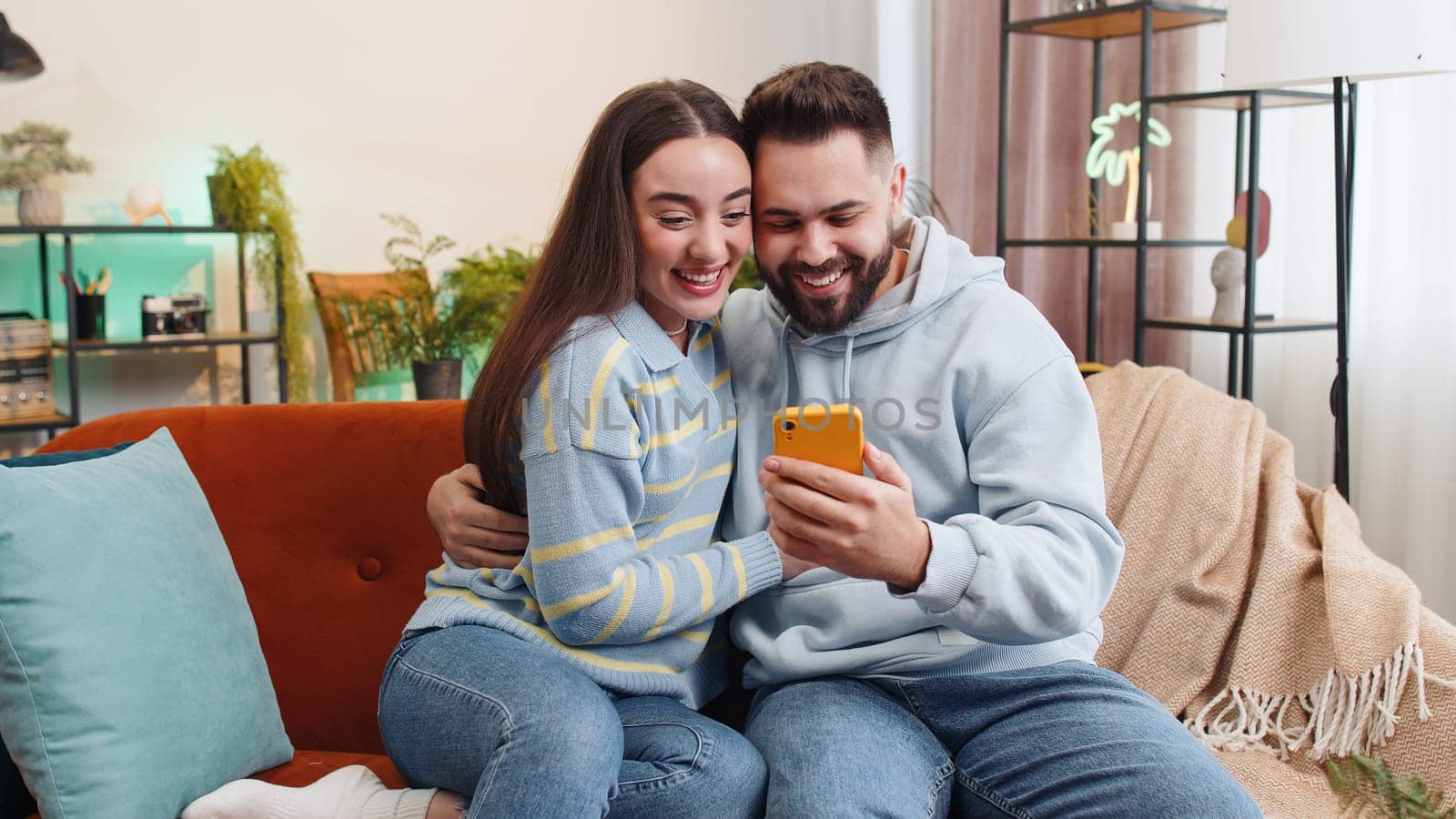 Family couple man woman use mobile smartphone found out great big win good news celebrate lottery jackpot lucky victory, playing game shopping online at home. Husband and wife together on sofa in room