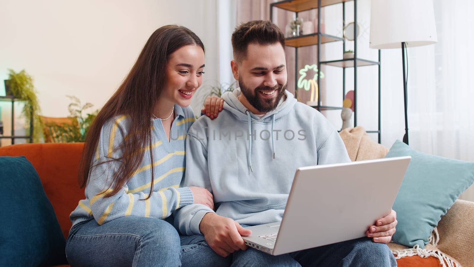 Young family marriage couple man woman making video laptop webcam conference call with friends or family, enjoying pleasant conversation at home. Husband wife laughing, waving hello on sofa in room