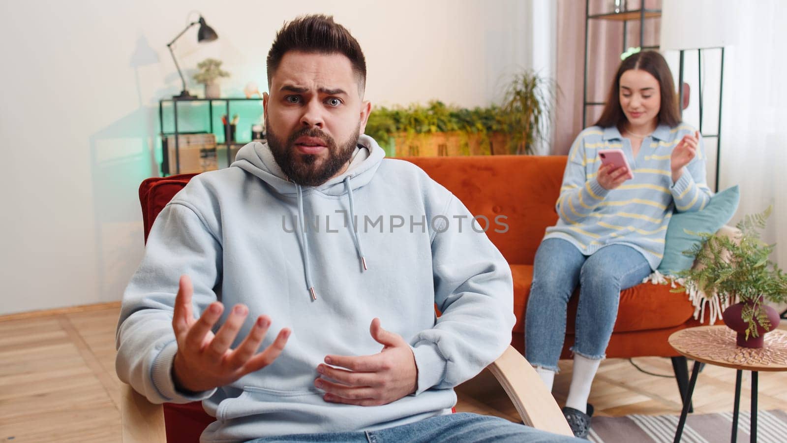 Unhappy man looking at camera, quarreling with woman addicted on online shopping wasting money with credit card, smartphone. Conflict problem, crisis in married family couple. Husband and wife at home