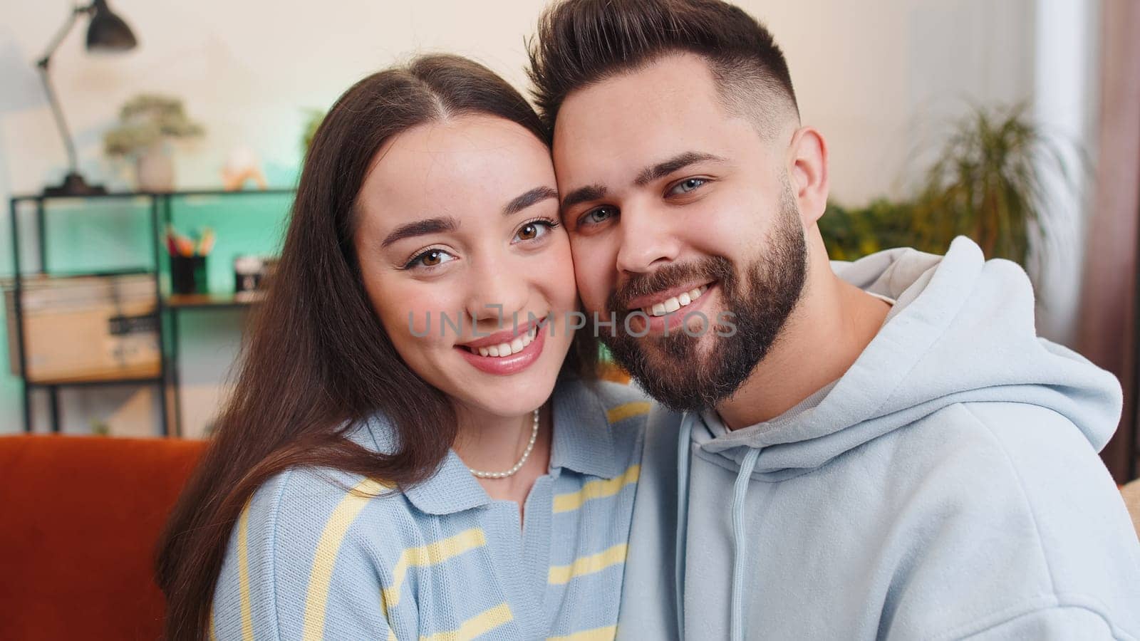 Portrait of happy smiling family marriage couple man woman looking at camera, hugging, embracing cheech to cheech at home. Attractive husband and wife laughing together on sofa in room. Domestic life