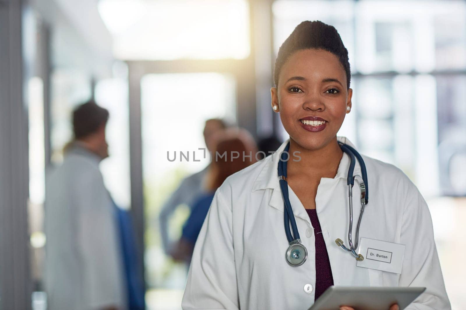 Quality healthcare is of utmost importance to me. Portrait of a young female doctor standing in a hospital with her colleagues in the background. by YuriArcurs