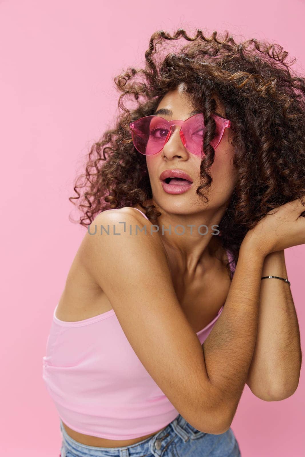 Happy woman afro curls hair dancing on pink background smile with teeth in summer pink t-shirt jeans and glasses, summer vibe, copy space by SHOTPRIME