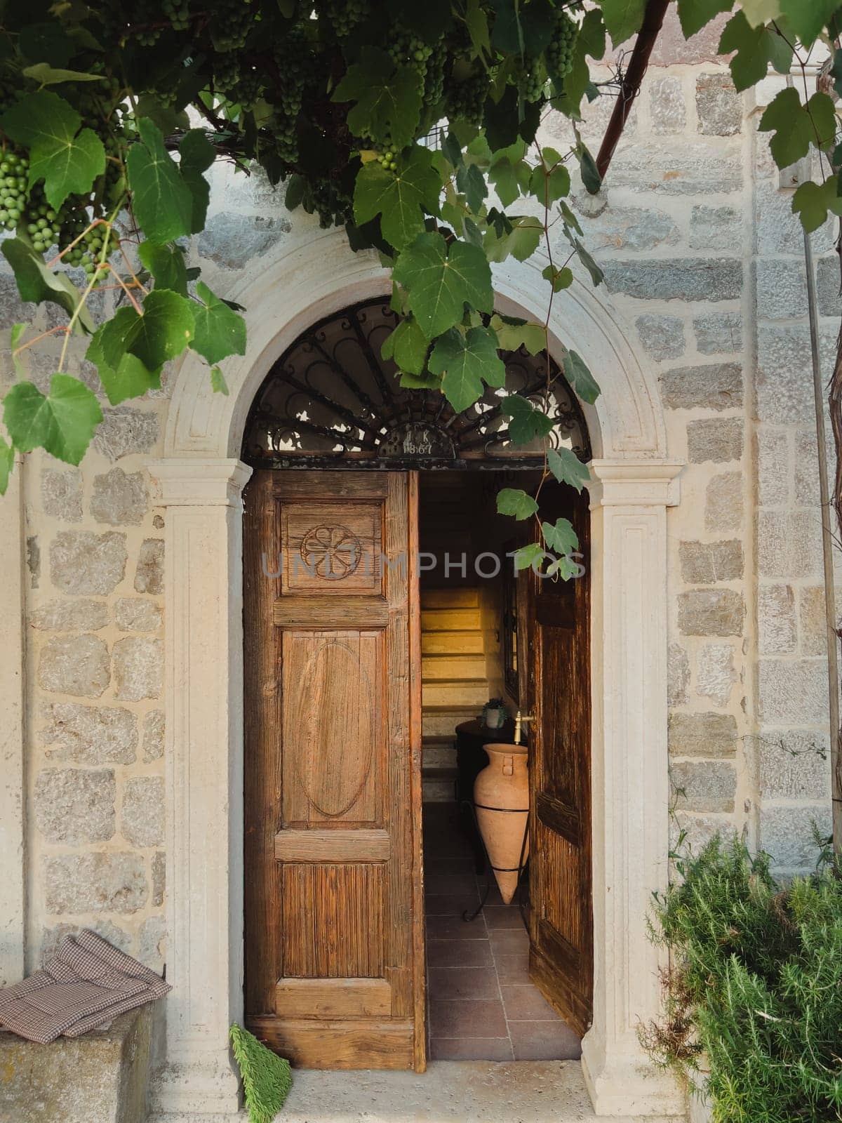 Green grapes weave over the arched entrance to an ancient building with a wooden door. High quality photo