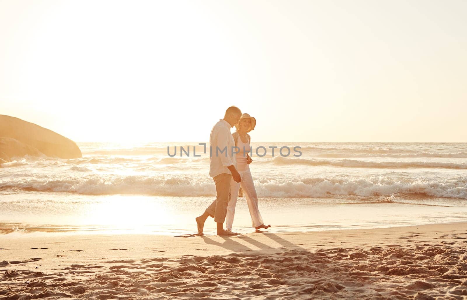 Romance never gets old. Full length shot of an affectionate middle aged couple walking hand in hand along the beach at sunset. by YuriArcurs
