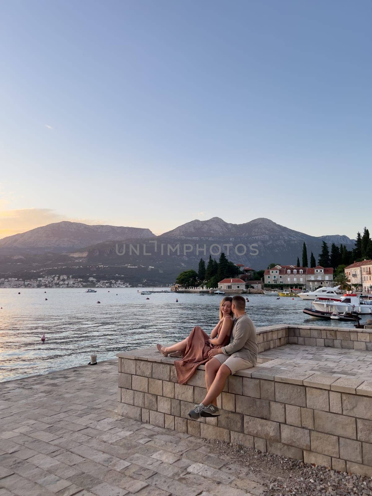 Man hugs woman, sitting on a stone fence on the shore of an old town. High quality photo