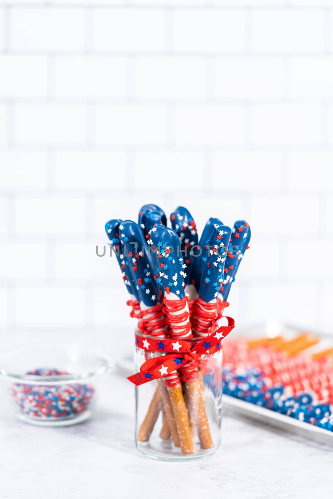 Homemade chocolate-covered pretzel rods decorated like the American flag in a glass jar.