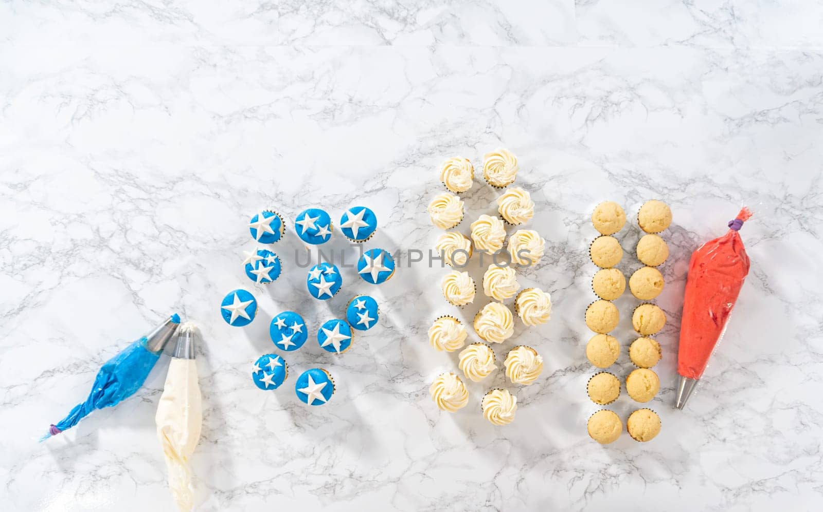 Flat lay. Frosting mini vanilla cupcakes with buttercream frosting to make an American flag mini cupcake cake.