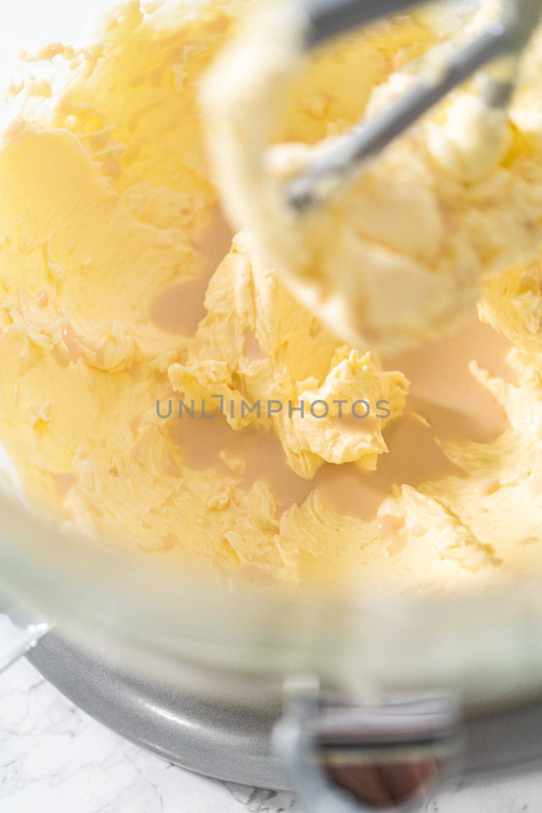 Whisking buttercream frosting in a glass mixing bowl with an electric kitchen mixer for American flag mini cupcakes.