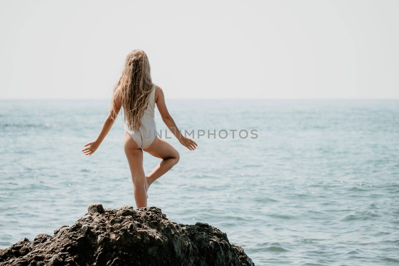 Woman and her daughter practicing balancing yoga pose on one leg up together on rock in the sea. Silhouette mother and daughter doing yoga at beach by panophotograph