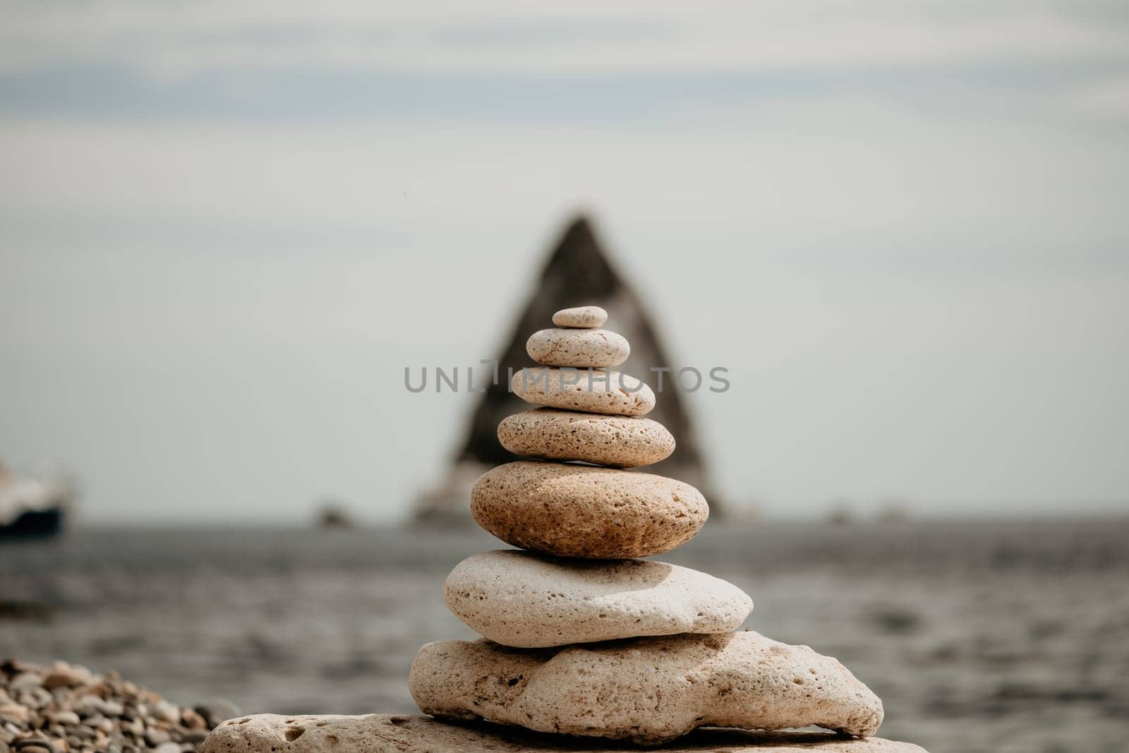 Pyramid stones on the seashore with warm sunset on the sea background. Happy holidays. Pebble beach, calm sea, travel destination. Concept of happy vacation on the sea, meditation, spa, calmness.