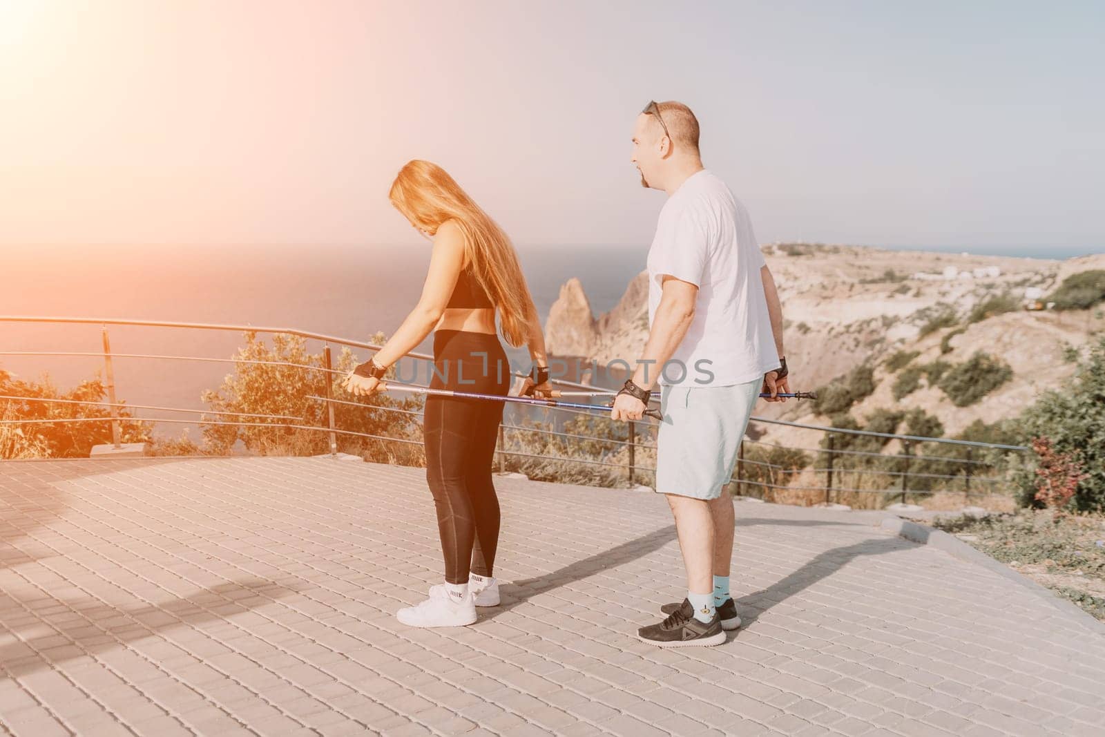 Happy Middle aged couple or friends practicing nordic walking in park near sea. Mature couple with trekking poles walking, practicing Nordic walking outdoors. Aging youthfully and sport concept.