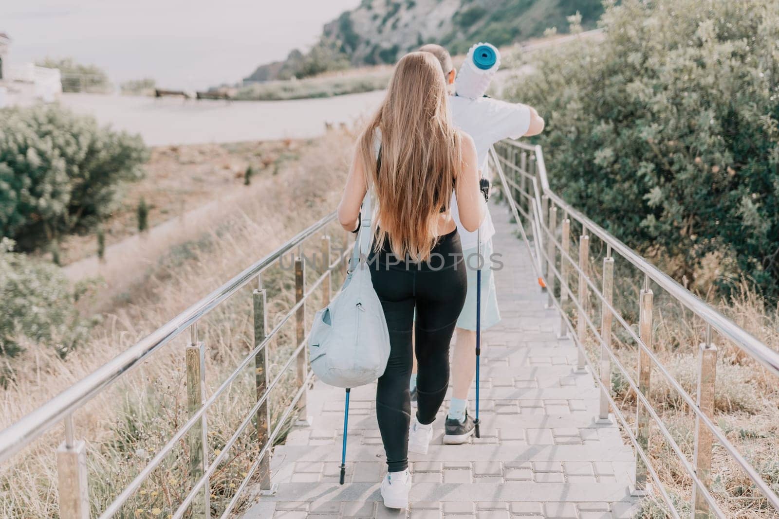 Happy Middle aged couple or friends practicing nordic walking in park near sea. Mature couple with trekking poles walking, practicing Nordic walking outdoors. Aging youthfully and sport concept.