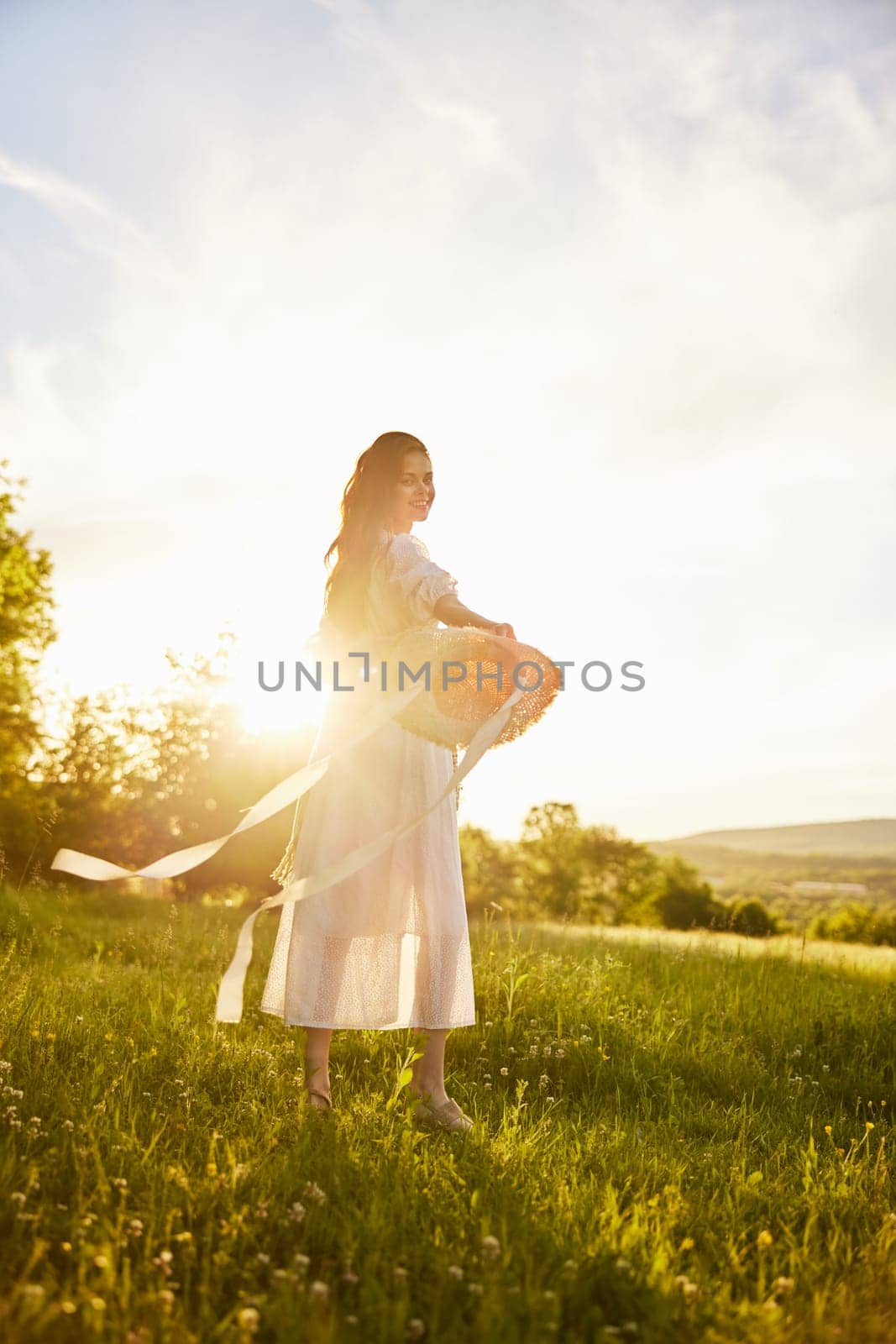 a woman in a light dress walks in nature holding a hat in her hands lit from the back by the sun. High quality photo