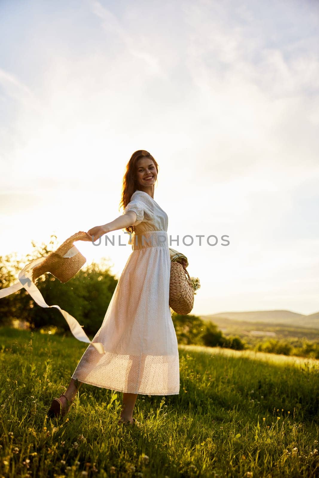 a woman in a light dress walks in nature holding a hat in her hands lit from the back by the sun. High quality photo