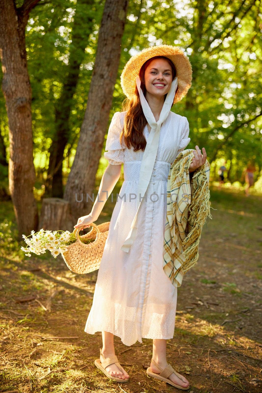 a happy woman in a light dress walks through the woods with a plaid and a wicker bag in her hands by Vichizh