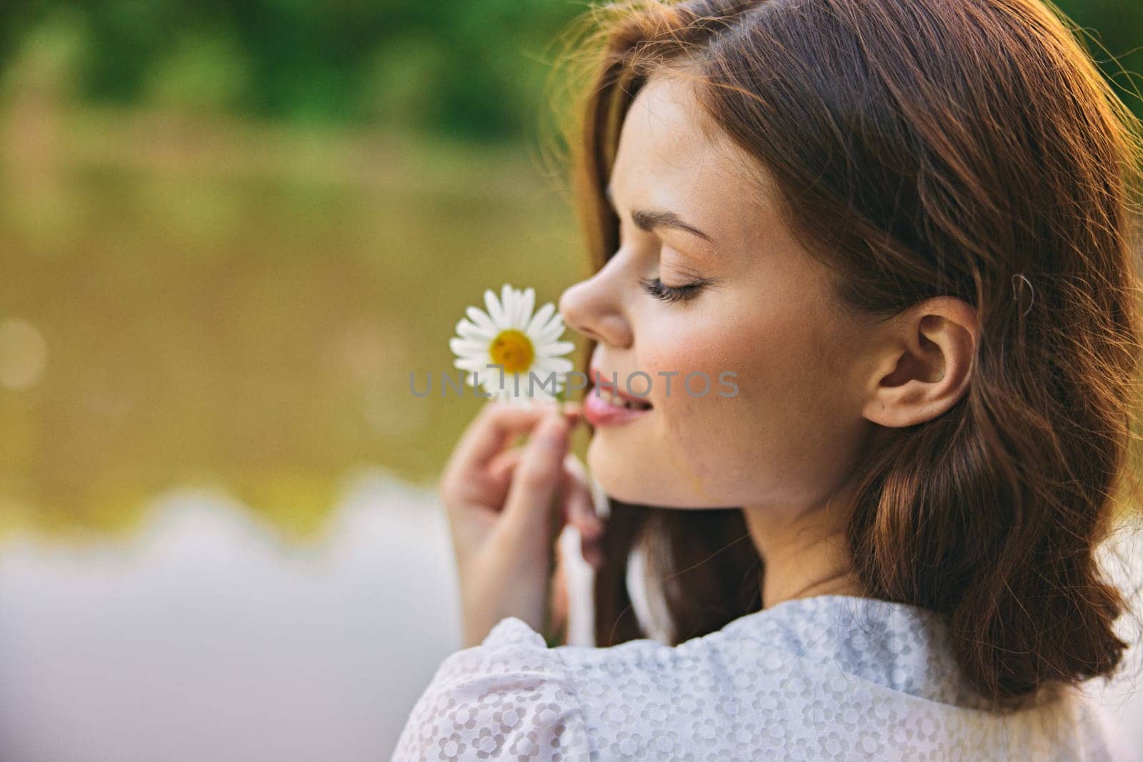 close-up portrait of a woman with a chamomile flower on the background of the lake. High quality photo