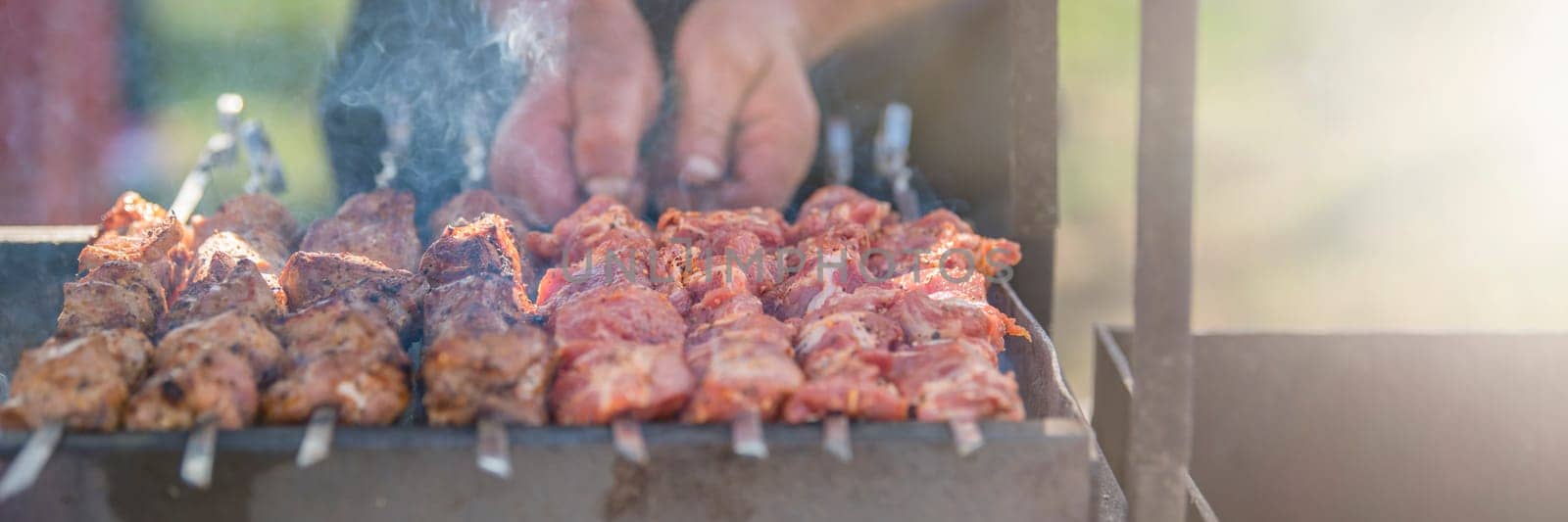 A man fries kebabs on skewers on a grill. Organization of a picnic in nature. by SERSOL