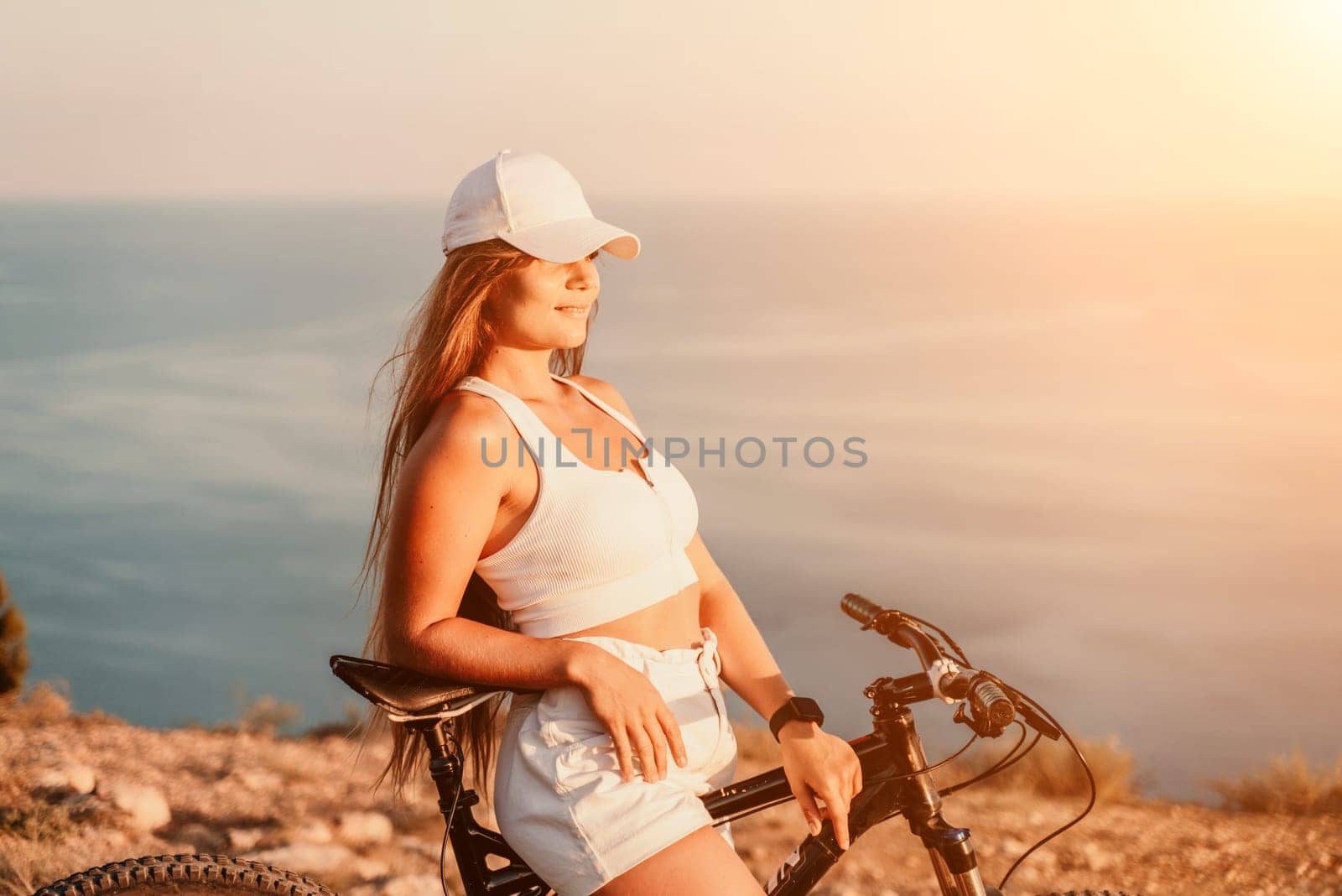 Woman travel bike sea. Happy woman cyclist sitting on her bike, enjoying the beautiful mountain and sea landscape, signifying the idea of an adventurous bike ride