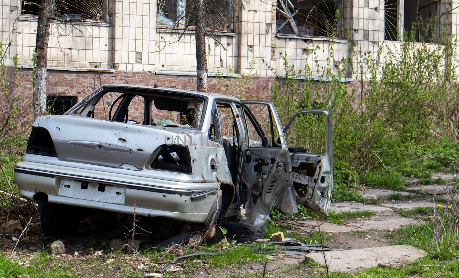 A broken car, shot by artillery, stands in the courtyard of a multi-storey residential building. War between Russia and Ukraine. The wreckage of an abandoned car