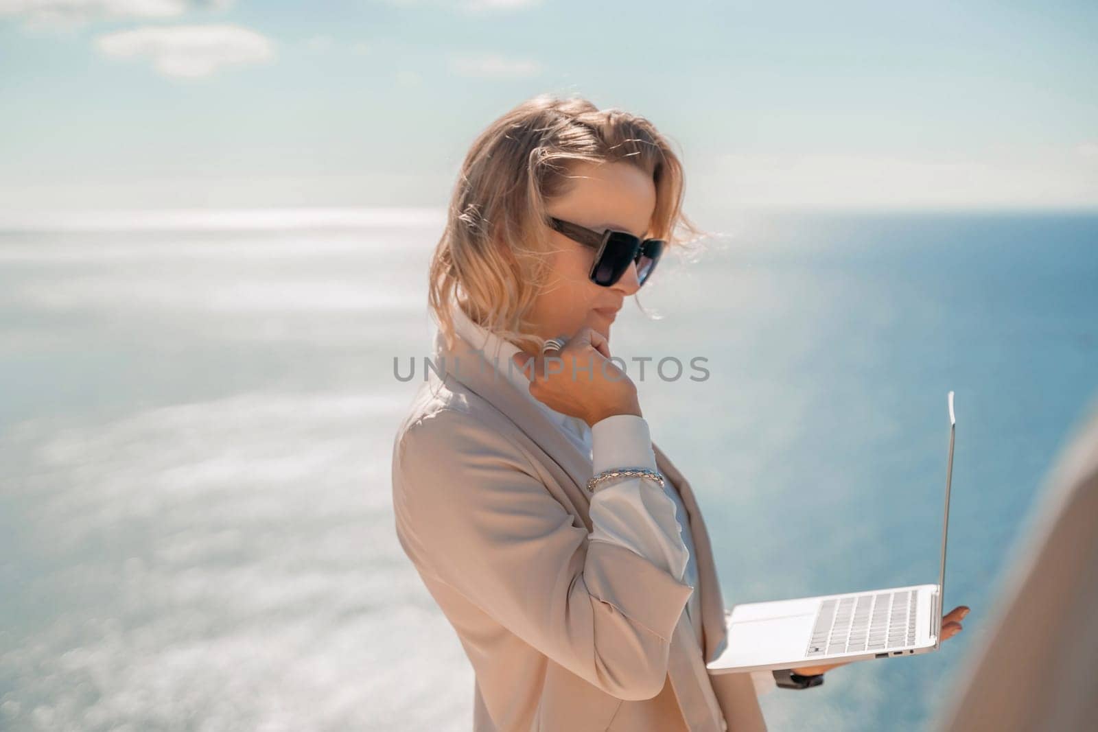 Freelance women sea working on the computer. Good looking middle aged woman typing on a laptop keyboard outdoors with a beautiful sea view. The concept of remote work