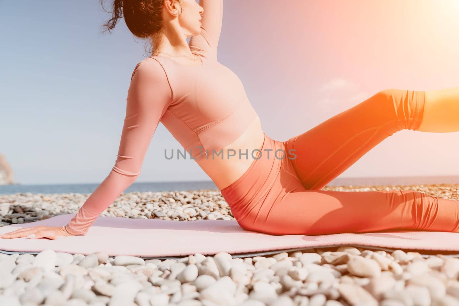 Middle aged well looking woman with black hair doing Pilates with the ring on the yoga mat near the sea on the pebble beach. Female fitness yoga concept. Healthy lifestyle, harmony and meditation.