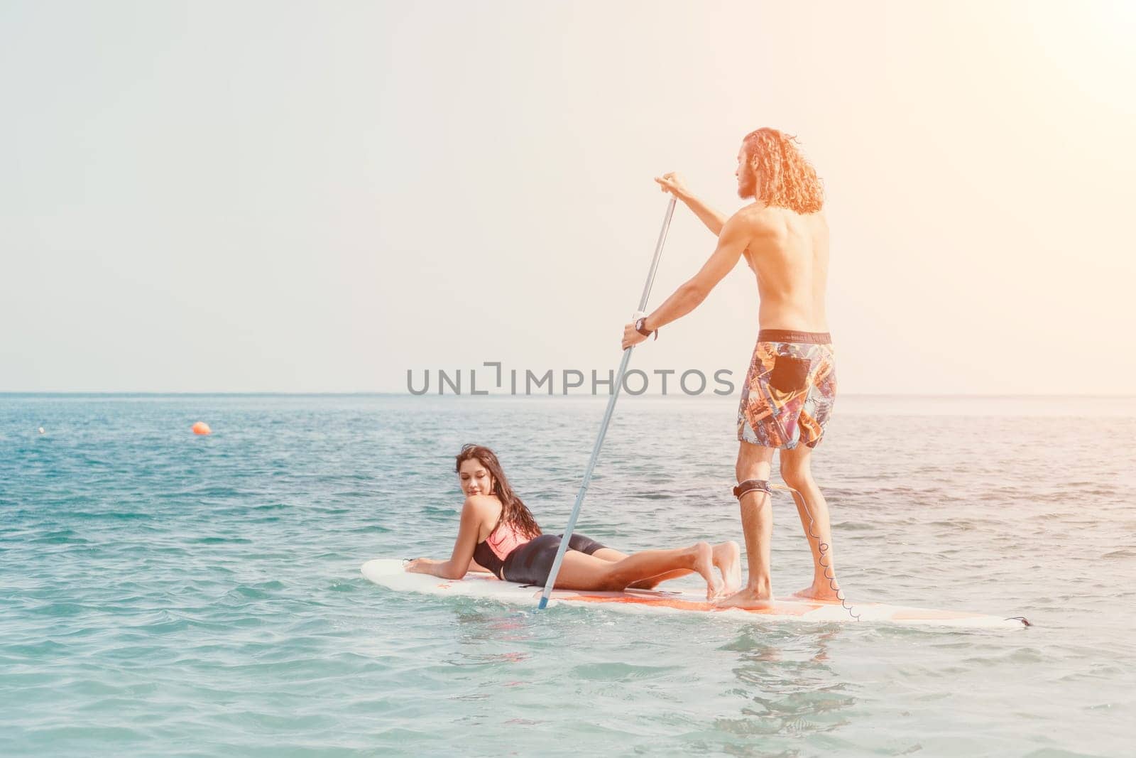 Silhouette of woman standing, surfing on SUP board, confident paddling through water surface. Idyllic sunset or sunrise. Sports active lifestyle at sea or river.